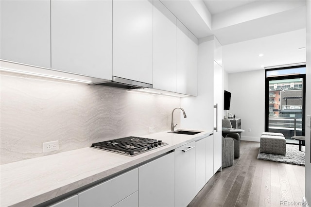 kitchen with light countertops, stainless steel gas stovetop, white cabinets, and a sink