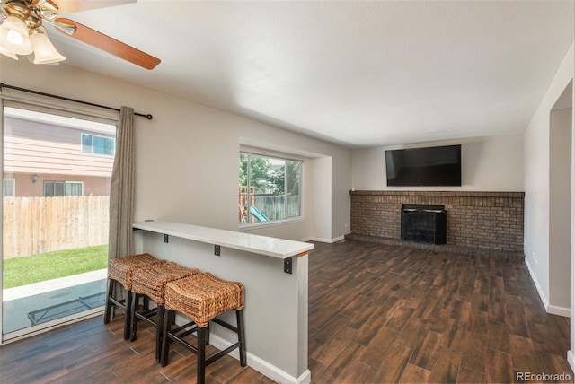 20445 Mitchell Pl, Denver, CO 80249 - kitchen with dark wood-style floors, a ceiling fan, a brick fireplace, a kitchen breakfast bar, and a peninsula