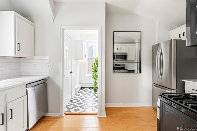 2098 N Clarkson St, Denver, CO 80205 - kitchen featuring appliances with stainless steel finishes, white cabinetry, baseboard heating, light wood-type flooring, and vaulted ceiling