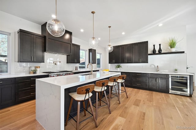 kitchen with sink, beverage cooler, light hardwood / wood-style floors, a kitchen island with sink, and a breakfast bar