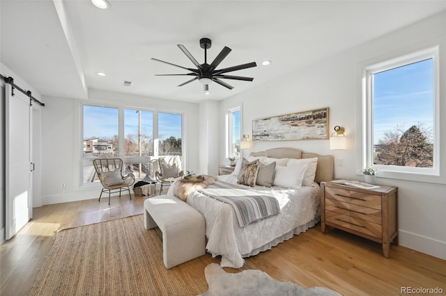 bedroom featuring ceiling fan, a barn door, and light hardwood / wood-style floors