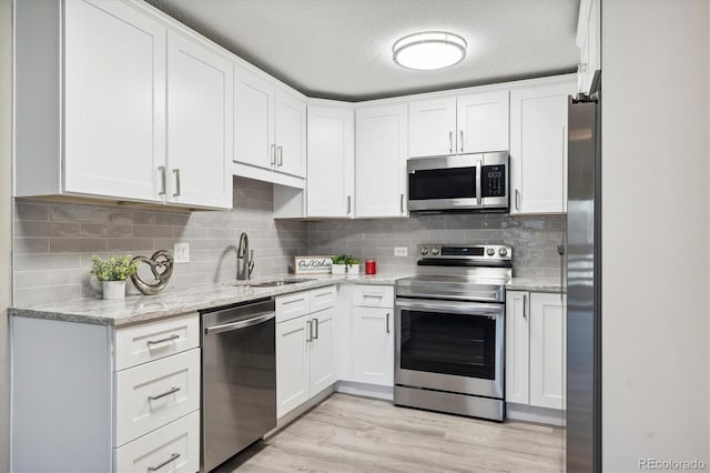 kitchen featuring sink, light hardwood / wood-style floors, light stone counters, white cabinetry, and stainless steel appliances