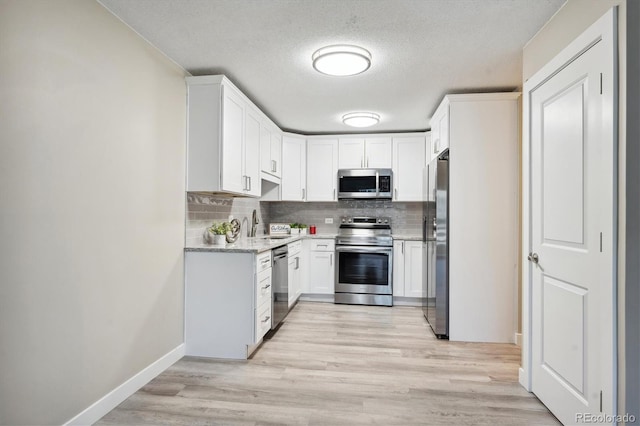 kitchen with light stone countertops, appliances with stainless steel finishes, tasteful backsplash, light hardwood / wood-style floors, and white cabinetry