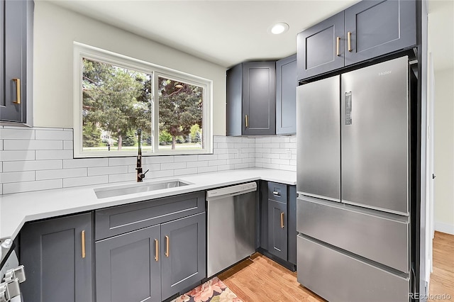 kitchen with stainless steel appliances, a sink, light countertops, backsplash, and light wood-type flooring