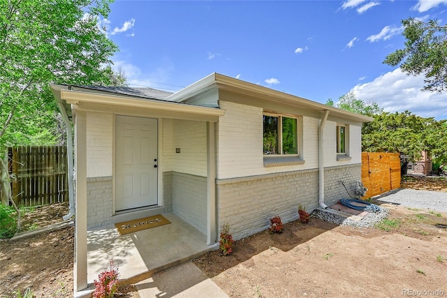 view of exterior entry with brick siding and fence