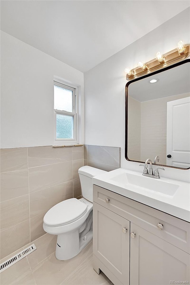 half bath with tile walls, toilet, vanity, a wainscoted wall, and tile patterned flooring