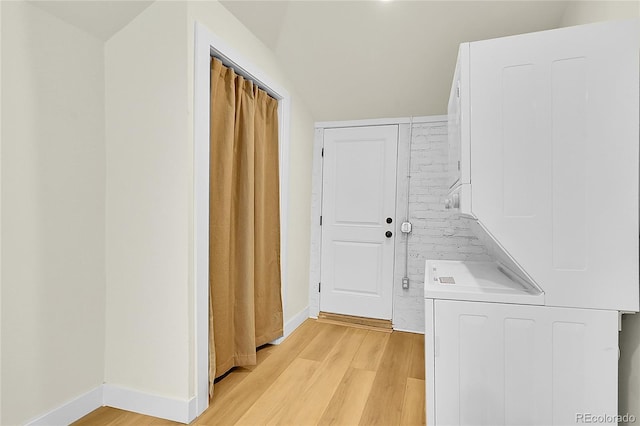 clothes washing area featuring stacked washer and clothes dryer, light wood finished floors, and baseboards