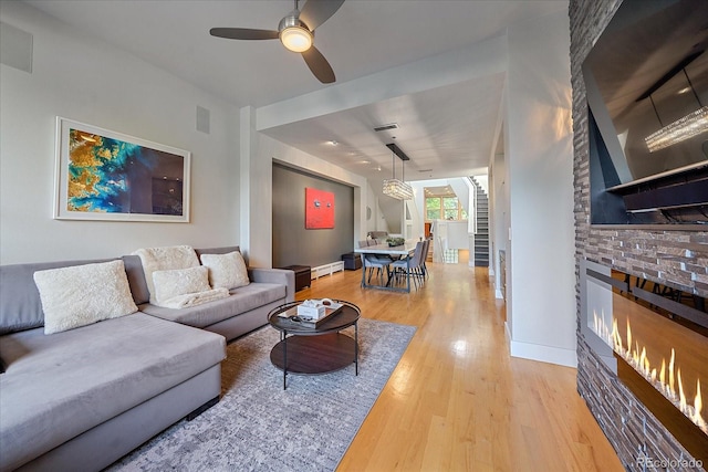 living room featuring baseboard heating, ceiling fan, wood-type flooring, and a fireplace