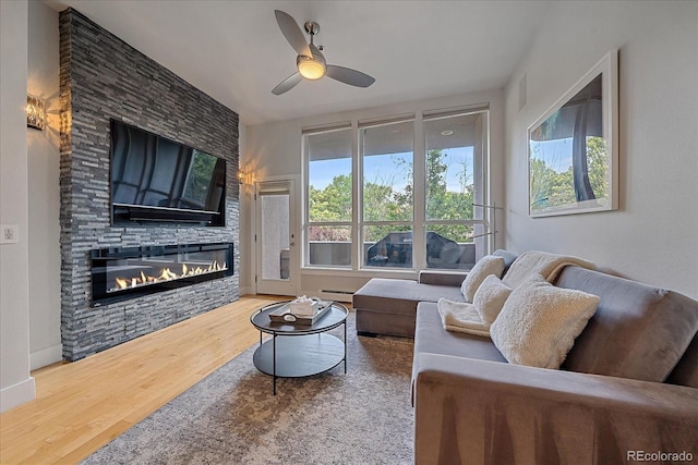 living room with hardwood / wood-style flooring, a stone fireplace, ceiling fan, and baseboard heating