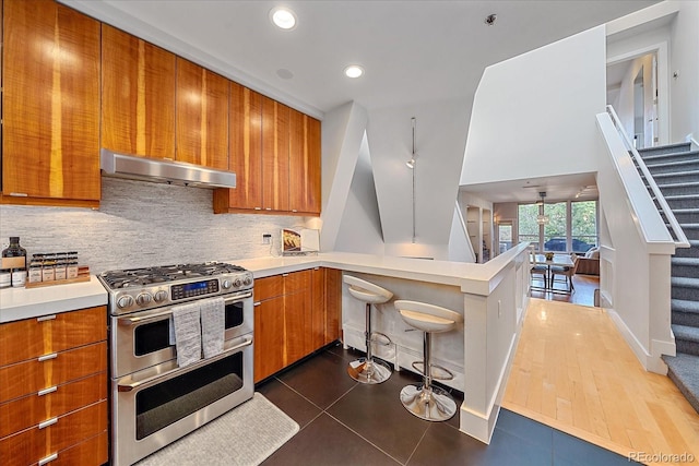 kitchen with double oven range, a kitchen breakfast bar, dark tile patterned flooring, kitchen peninsula, and decorative backsplash