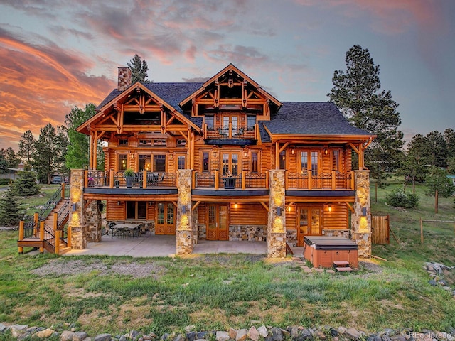 back house at dusk with a yard, a patio area, a hot tub, and a balcony