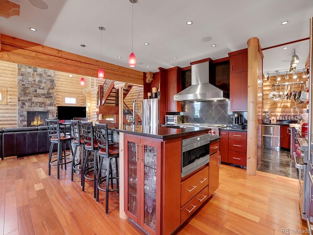 kitchen featuring pendant lighting, rustic walls, a center island, stainless steel appliances, and wall chimney exhaust hood