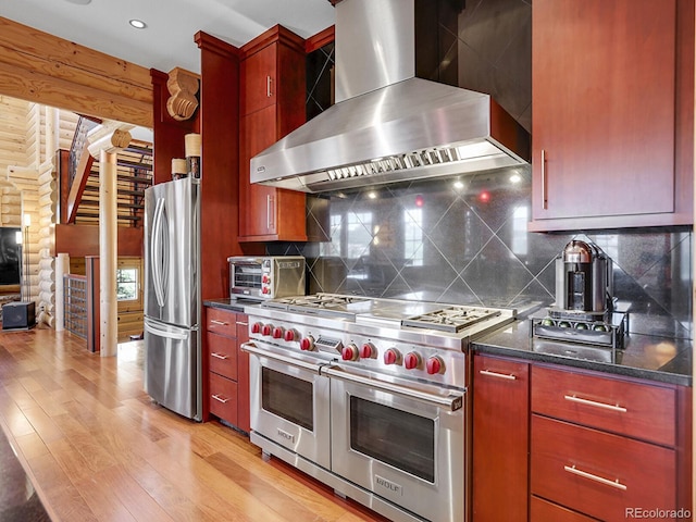 kitchen with wall chimney range hood, backsplash, stainless steel appliances, log walls, and light wood-type flooring