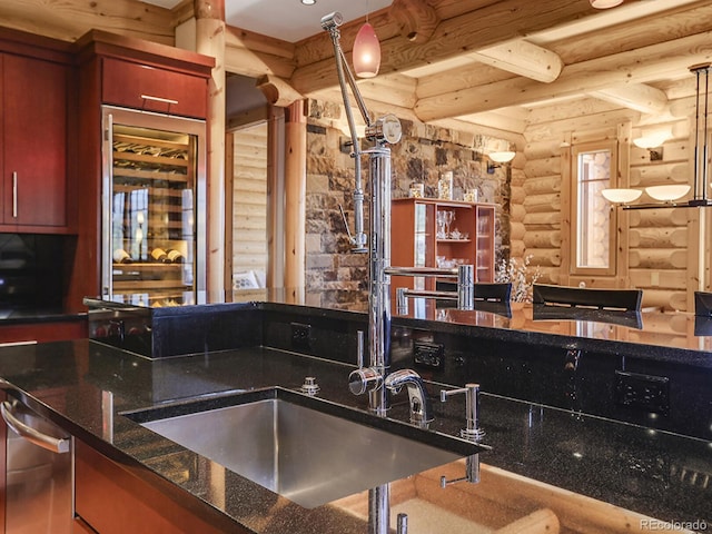 kitchen with dishwasher, rustic walls, dark stone countertops, hanging light fixtures, and beam ceiling