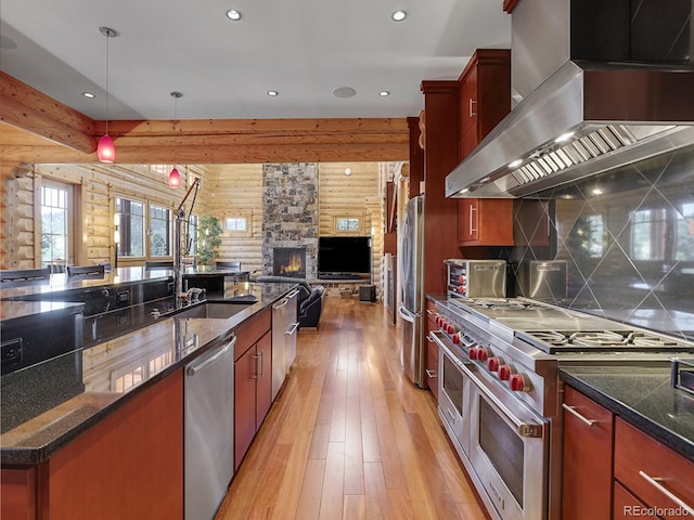 kitchen with pendant lighting, sink, appliances with stainless steel finishes, ventilation hood, and log walls