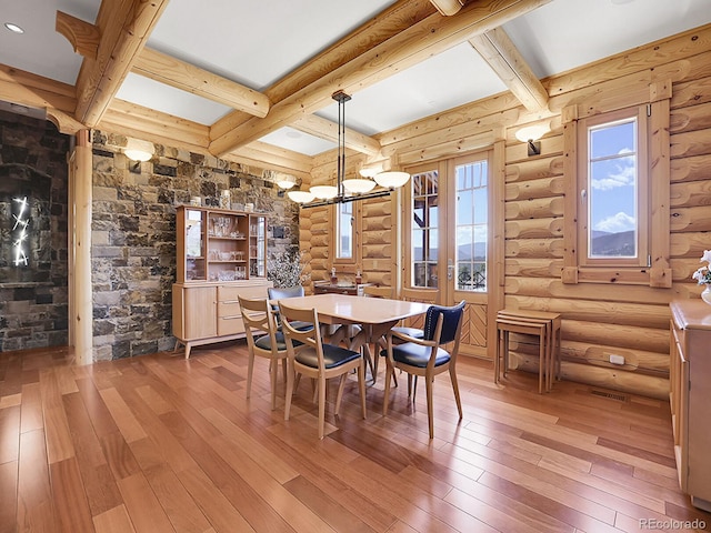 dining area with a notable chandelier, wood-type flooring, rustic walls, and beamed ceiling