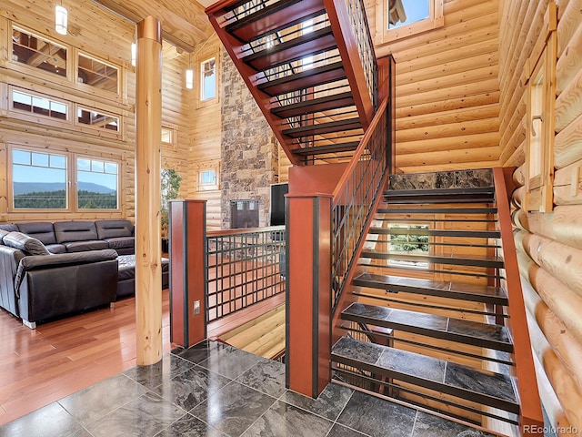 stairs with hardwood / wood-style flooring, plenty of natural light, a towering ceiling, and rustic walls