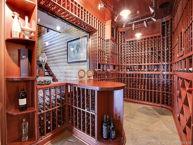 wine room featuring wood ceiling, log walls, and rail lighting