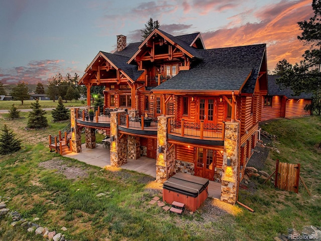 back house at dusk featuring a hot tub, a patio, a wooden deck, and a lawn