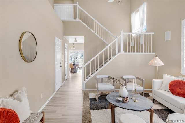 living room featuring stairs, a high ceiling, baseboards, and wood finished floors