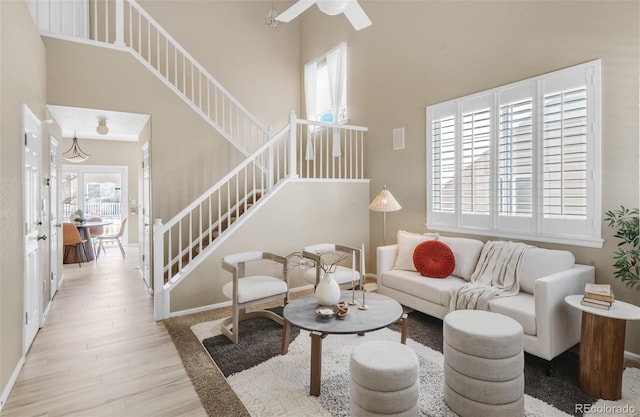 living room featuring stairway, a towering ceiling, a ceiling fan, wood finished floors, and baseboards