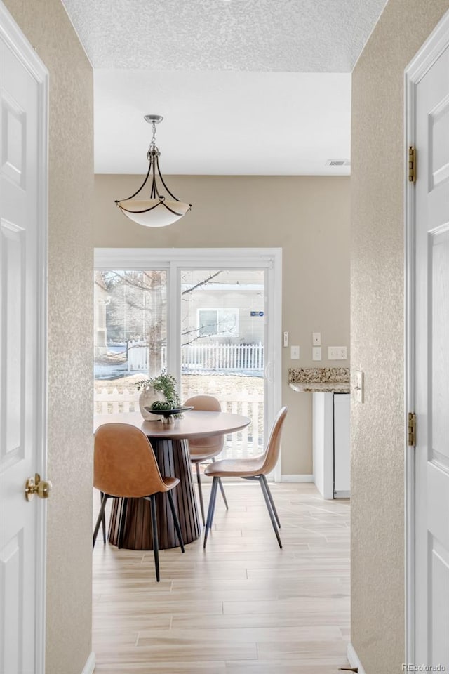 dining area featuring a textured wall, a textured ceiling, and light wood finished floors