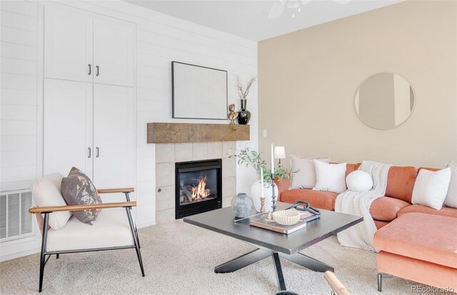 carpeted living room with ceiling fan, a tile fireplace, and visible vents