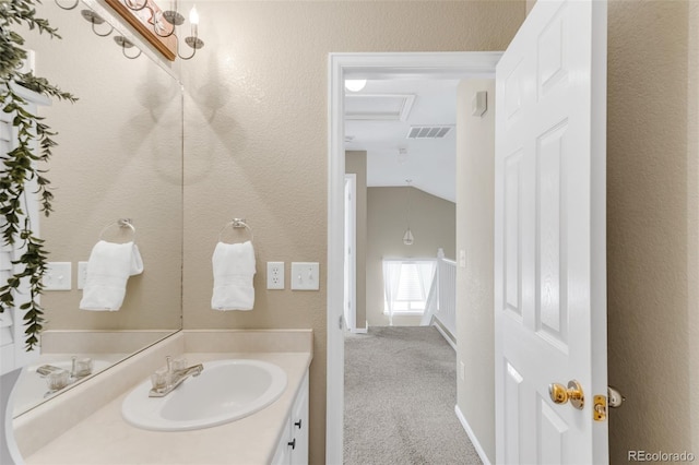 bathroom featuring lofted ceiling, a textured wall, visible vents, and vanity