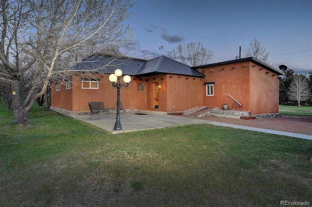 back house at dusk with a patio area and a yard