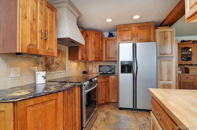 kitchen featuring appliances with stainless steel finishes, backsplash, light tile flooring, custom range hood, and dark stone counters