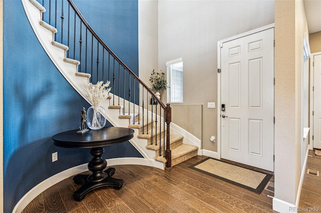 entrance foyer featuring a towering ceiling, stairway, baseboards, and wood finished floors