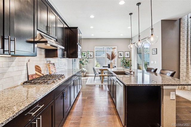 kitchen featuring decorative backsplash, dark wood-style floors, light stone counters, stainless steel appliances, and a sink