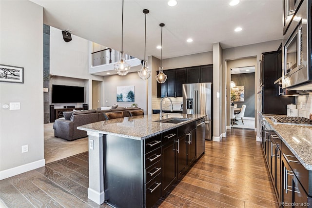 kitchen featuring dark wood-style floors, tasteful backsplash, appliances with stainless steel finishes, open floor plan, and a sink