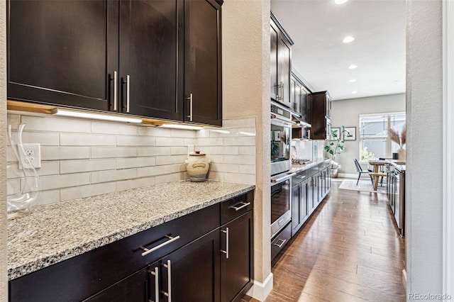 kitchen with dark wood-type flooring, oven, dark brown cabinetry, and light stone countertops