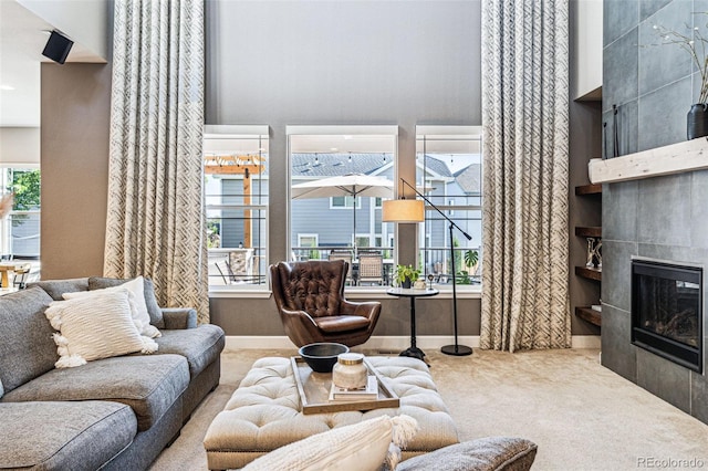 living area with carpet floors, a healthy amount of sunlight, a fireplace, and a towering ceiling