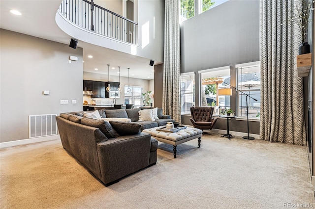 living area featuring light carpet, a towering ceiling, visible vents, and baseboards