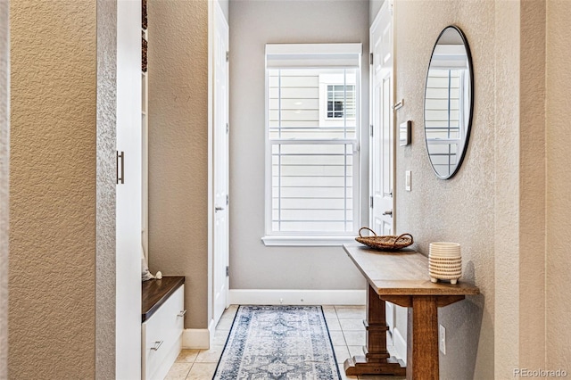 doorway to outside featuring light tile patterned floors, a textured wall, and baseboards