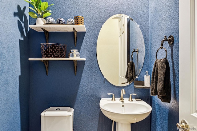 bathroom with toilet, a sink, and a textured wall