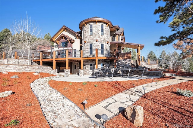 back of property featuring a patio, a balcony, and stone siding