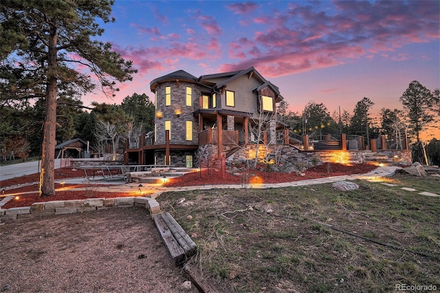 back of house at dusk featuring stairs, a patio area, stone siding, and an outdoor fire pit
