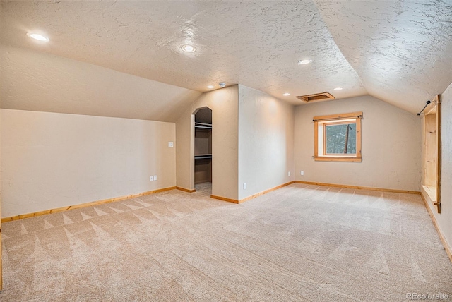 bonus room featuring carpet floors, a textured ceiling, baseboards, lofted ceiling, and visible vents