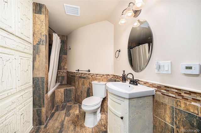 bathroom with visible vents, toilet, tile walls, a wainscoted wall, and vaulted ceiling