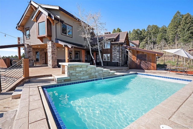 back of house with a patio area, an outdoor pool, and stone siding