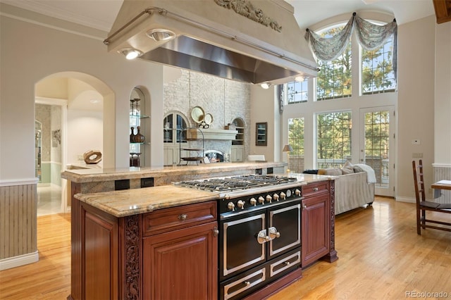 kitchen featuring a high ceiling, crown molding, light wood-type flooring, double oven range, and light stone counters