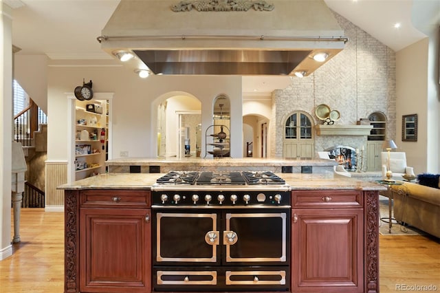 kitchen with vaulted ceiling, ornamental molding, a fireplace, range with two ovens, and light hardwood / wood-style floors