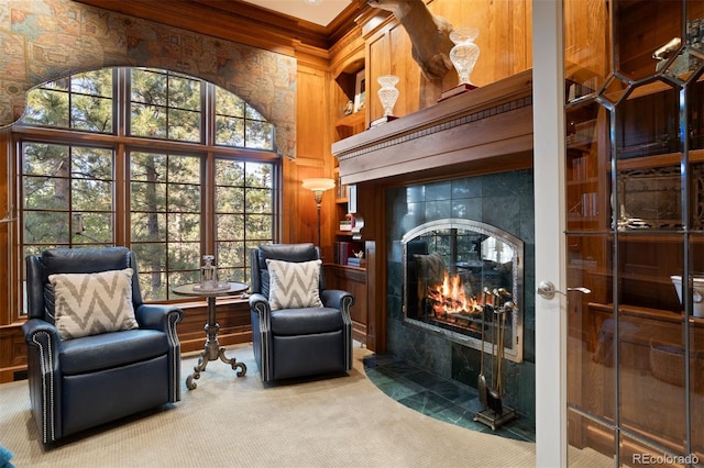 sitting room featuring a high ceiling, wooden walls, a tile fireplace, crown molding, and carpet floors