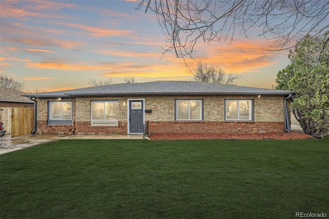 ranch-style home featuring brick siding, roof with shingles, a front yard, and fence