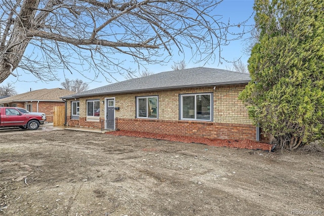 ranch-style home featuring driveway, brick siding, and roof with shingles