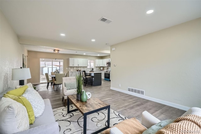 living room with light wood-style floors, baseboards, visible vents, and recessed lighting