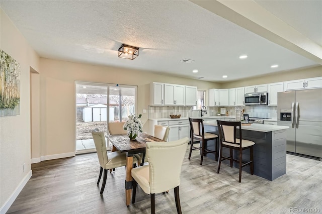 dining space featuring light wood-style flooring, visible vents, baseboards, and a textured ceiling